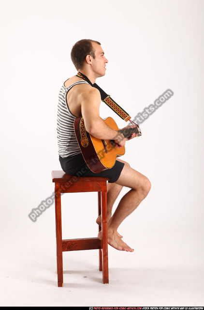 Stylish content woman thoughtfully playing guitar sitting on ground with  crossed legs stock photo - OFFSET