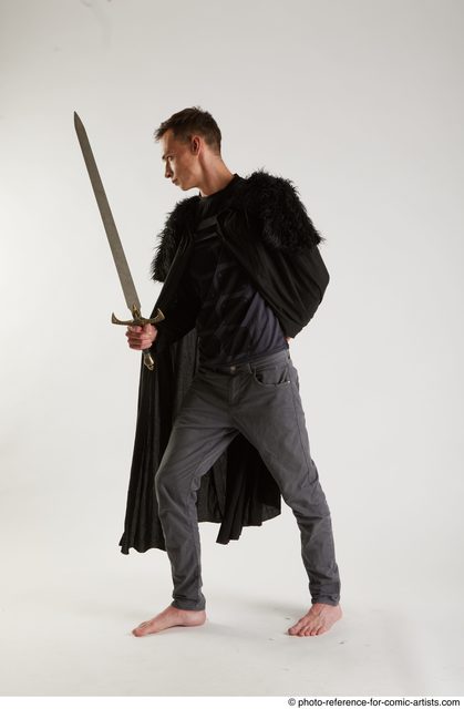 full length portrait of a pretty brunette girl wearing a black shirt and  leather boots, holding a sword. Standing pose facing away and holding a  sword, on a grey studio background. Stock